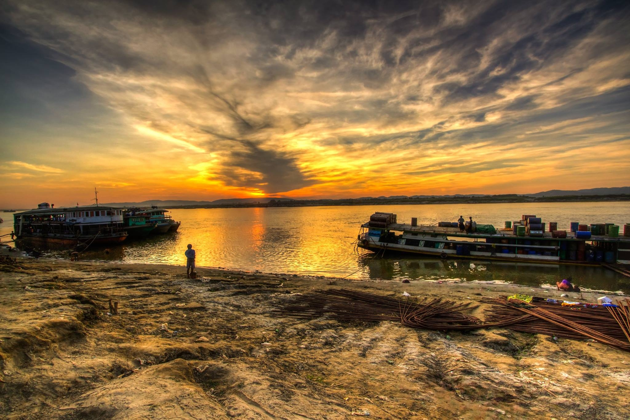 A man observes the stationed boats by the river with the sunset in the background